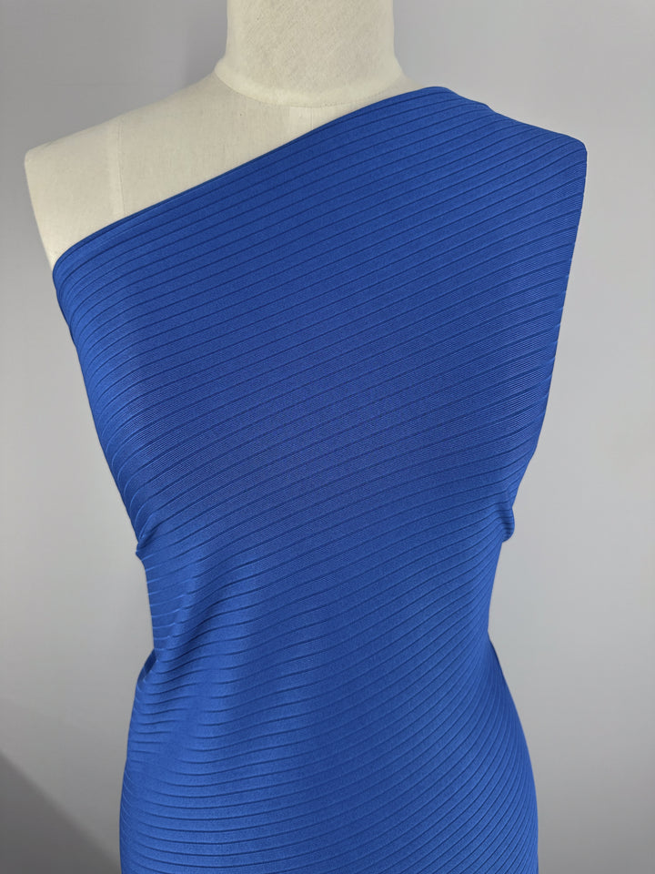 A mannequin displays the "Rib Knit - Classic Blue - 170cm" by Super Cheap Fabrics, highlighting the allure of medium weight rib knit fabric. The textured knit creates a diagonal pattern across the torso, set against a neutral background.