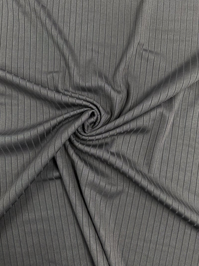 The Rib Knit - Dark Grey - 170cm from Super Cheap Fabrics is shown in a close-up spiral arrangement, displaying its medium weight and subtle sheen that highlights the intricate textured pattern and linear folds.