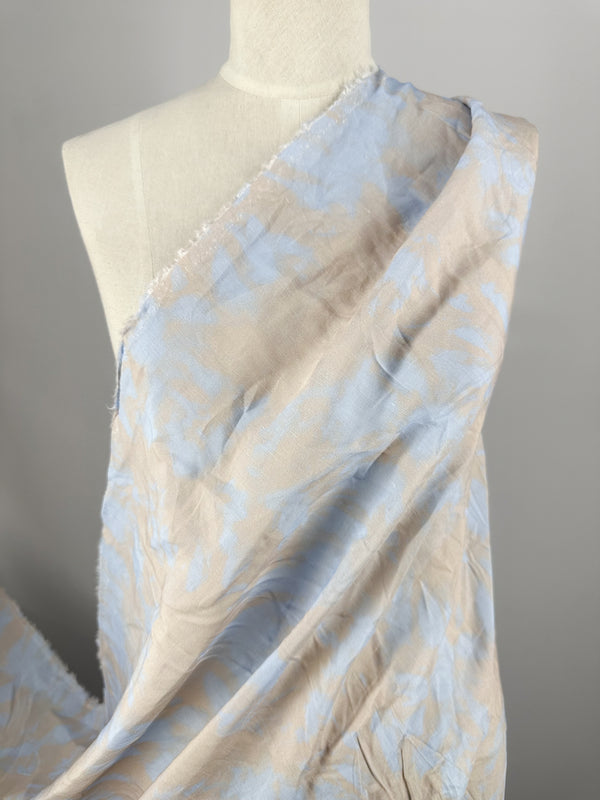 A mannequin is draped with Super Cheap Fabrics' Linen Viscose in Blue Bell, showcasing a light beige and soft blue floral pattern. The luxurious 140cm fabric loosely hangs around the shoulder, reminiscent of fancy dresses against a plain background, highlighting its limited stock allure.