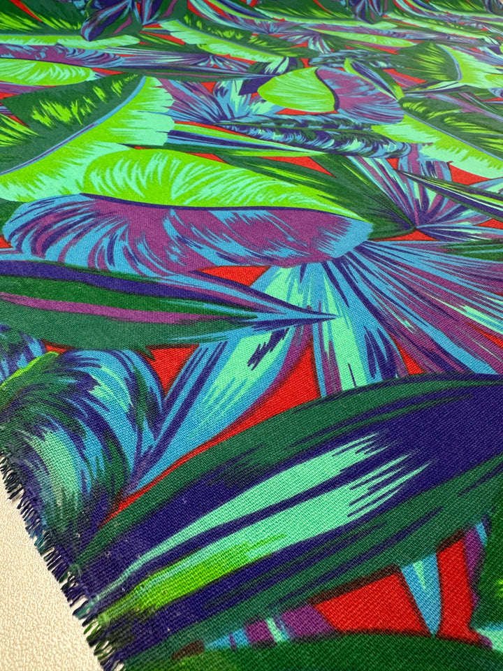 The Cotton Duck - Palm Lush Meadow from Super Cheap Fabrics is a vibrant 140cm medium-weight fabric featuring a bold tropical leaf pattern in green, blue, purple, and hints of red. Overlapping leaves create a jungle-inspired look ideal for stylish home décor projects.