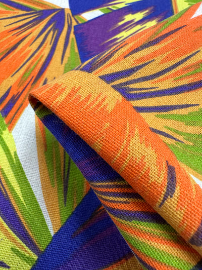 Close-up of Cotton Duck by Super Cheap Fabrics in "Palm Nectarine," a vibrant 140cm medium-weight fabric. It features an abstract pattern with orange, purple, green, and blue brushstrokes, slightly folded to display its texture—ideal for bold home décor projects.