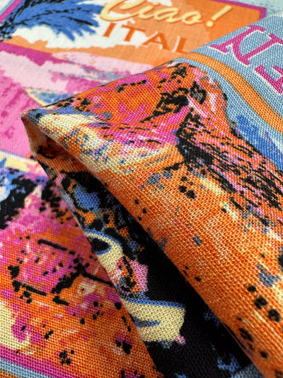 Super Cheap Fabrics' Bamboo Rayon - Italiano (145cm) is a colorful, textured, lightweight fabric with bold orange, pink, and blue abstract prints. It features text like "Ciao!" and "Italy" and is showcased in a folded position.