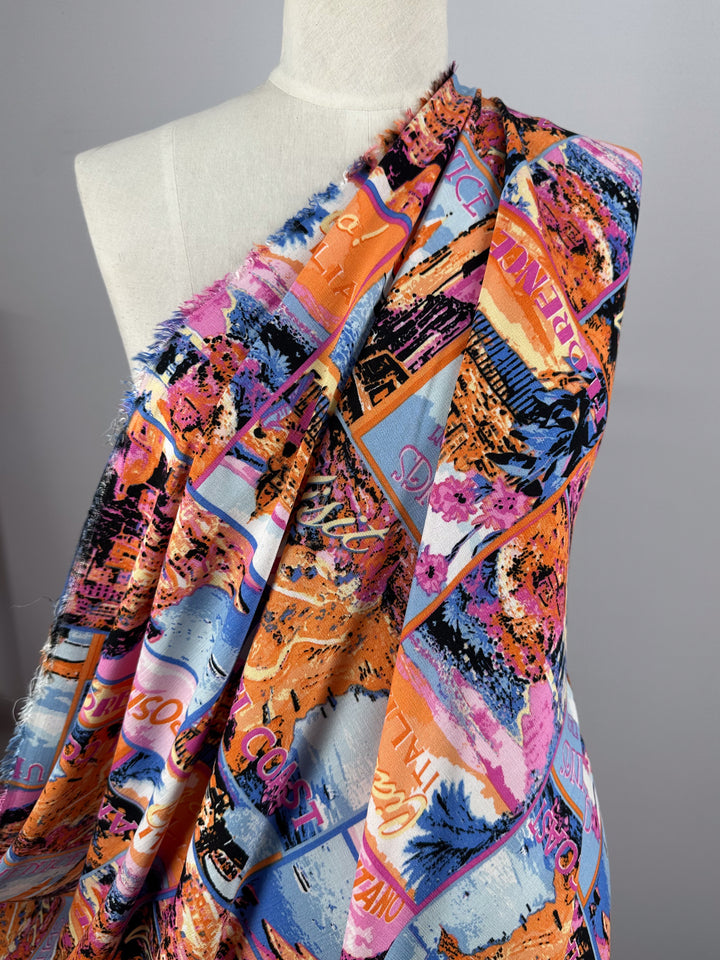 The Bamboo Rayon - Italiano by Super Cheap Fabrics is a lightweight fabric showcasing a vibrant abstract cityscape in pink, purple, blue, orange, and black draped on a white mannequin. Featuring stylized buildings and landscapes, it's ideal for versatile projects. Width: 145cm.