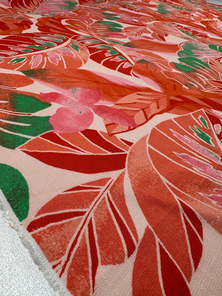 A close-up of Super Cheap Fabrics' Bamboo Rayon - Grapefruit Jungle features a vibrant, lightweight fabric with bold, overlapping leaf patterns in red, pink, and green. It has a soft woven texture and creates a dynamic tropical vibe on a light background—ideal for beginner-friendly sewing projects.