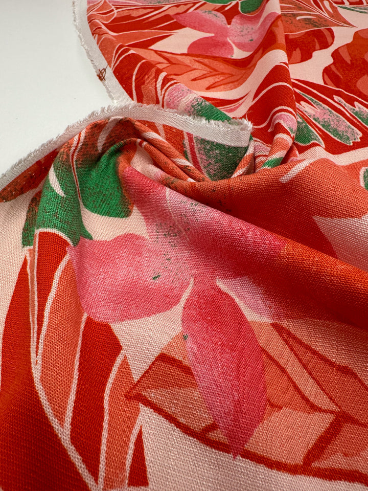 Close-up of Bamboo Rayon - Grapefruit Jungle by Super Cheap Fabrics, a colorful, lightweight fabric with a floral design in red, pink, and green. Made from bamboo rayon, it drapes beautifully with slight wrinkles showing its texture. The edge is visible at the top, ideal for beginners.