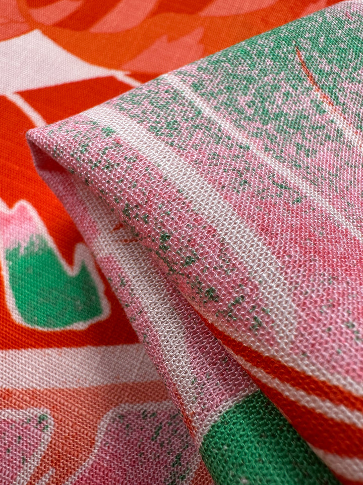 Close-up of the folded, lightweight Bamboo Rayon - Grapefruit Jungle fabric by Super Cheap Fabrics shows vibrant patterns in pink, green, and red abstract designs. The visible weave adds tactile quality to the vivid colors, making it ideal for beginner-friendly sewing projects.