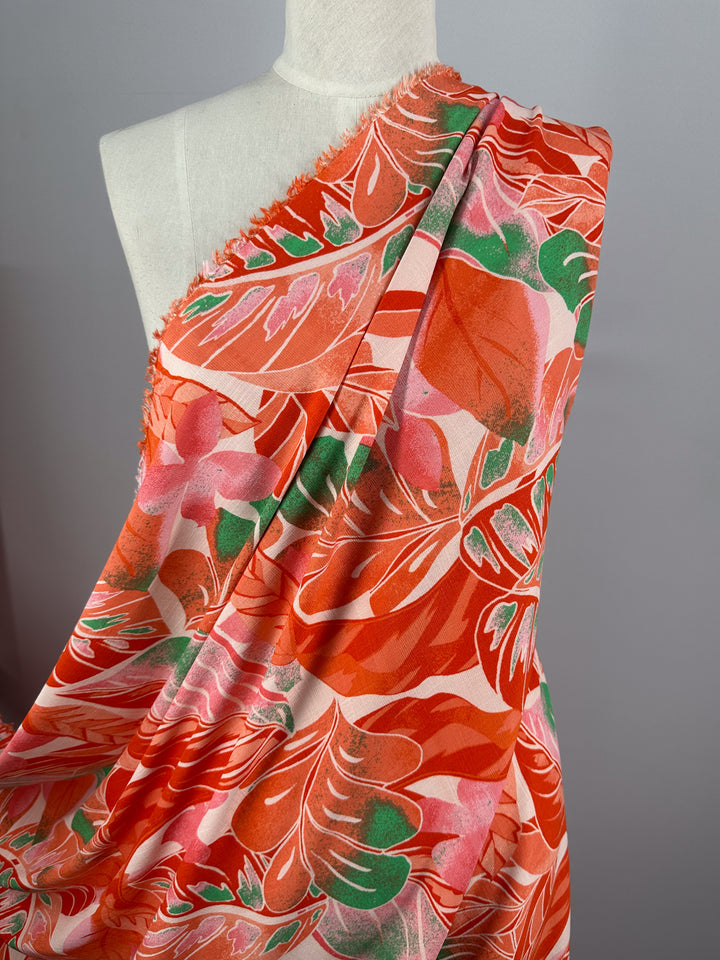 A mannequin displays Super Cheap Fabrics' Bamboo Rayon - Grapefruit Jungle, a vibrant lightweight fabric with a red, pink, and green floral pattern on a white background. The diagonal arrangement showcases its bold design, ideal for beginner-friendly sewing projects.