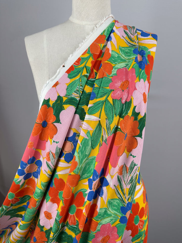 A mannequin showcases Super Cheap Fabrics' Bamboo Rayon - Florita - 145cm, featuring a lively, lightweight fabric with red, pink, orange, and blue flowers and green leaves on a light background. The colorful floral pattern creates an eye-catching appearance.