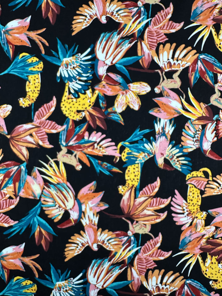 Super Cheap Fabrics' Linen Blend - Paradiso Black features a vibrant abstract pattern of stylized flowers and leopards in bold blue, orange, pink, and yellow hues on a black background, offering a dynamic visual effect. Width: 135cm.