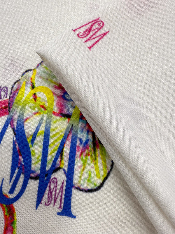 Close-up of Super Cheap Fabrics' Viscose Knit - Orchid (135cm), featuring breathable white fabric with vibrant, artistic prints and overlapping "SM" letters in blue, red, and yellow; fabric is slightly folded to show design details.