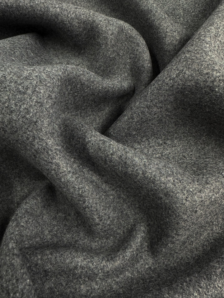 A close-up of the Super Cheap Fabrics' Melton Wool in Charcoal Marle, featuring a textured, slightly rough surface. The heavy-weight 150cm wool fabric is crumpled with gentle folds and shadows for a plush, cozy appearance that's perfect for crafting elegant skirts.