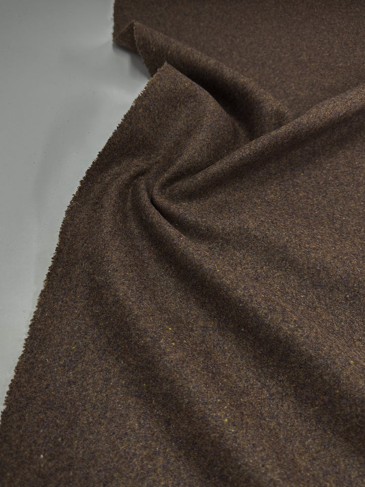 The Melton Wool - Multi Marle by Super Cheap Fabrics is a heavy wool fabric in rich brown, showcased on a light gray background. It's slightly twisted and gathered, forming soft folds and shadows reminiscent of flowing skirts.