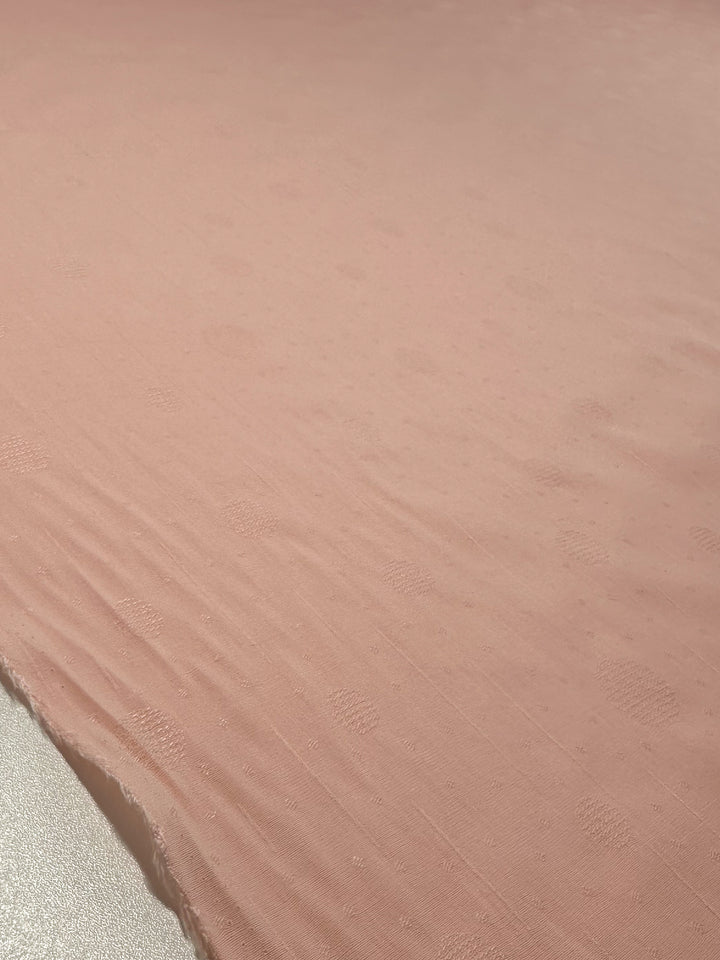 A large piece of Super Cheap Fabrics' Textured Cotton - Silver Pink - 143cm is spread smoothly, showcasing its extra lightweight 100% cotton. Under soft lighting, the subtle dotted texture and delicate weave are highlighted beautifully.