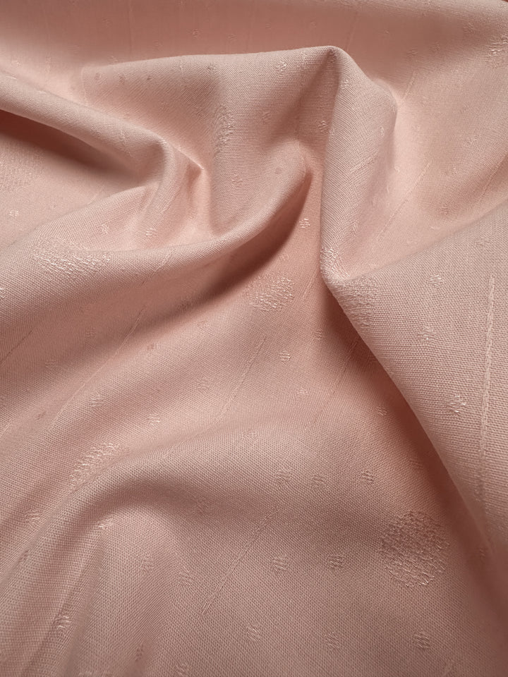 A close-up of the Super Cheap Fabrics' Textured Cotton in Silver Pink (143cm) showcases its subtle pattern. The 100% cotton material looks slightly wrinkled, with the light accentuating its intricate weave and texture.