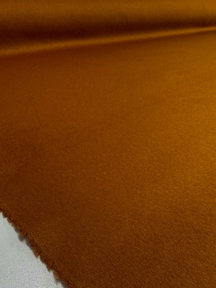 A close-up of Super Cheap Fabrics' Wool Cashmere in Roasted Pecan (150cm), a rich burnt orange, heavyweight fabric with a soft texture, displayed smoothly on a surface and gently curling at one edge.