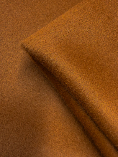 Close-up of Super Cheap Fabrics' Wool Cashmere in Roasted Pecan (150cm): luxurious, brown-orange fabric with a fuzzy texture, gentle folds, and a smooth, velvety finish.
