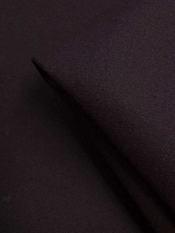 A close-up of folded Wool Cashmere - Gothic Grape by Super Cheap Fabrics (150cm), showcasing its extra heavy weight, dark grape hue, and soft, slightly textured surface with gentle shadows that highlight its luxurious thickness.