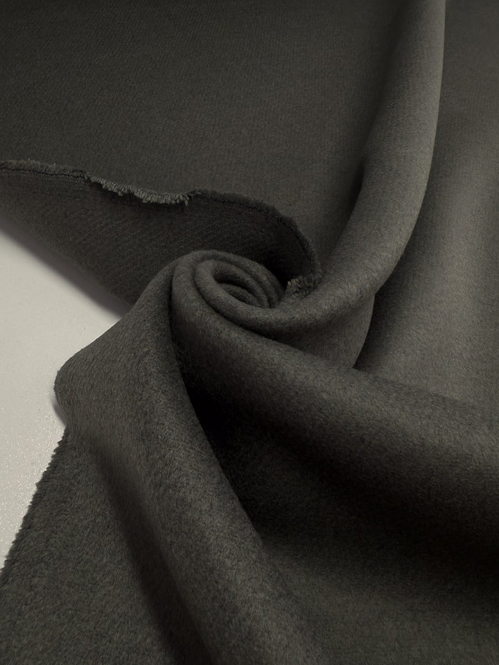 A close-up of Super Cheap Fabrics’ Wool Cashmere in Agave Green (150cm): extra heavy weight, soft texture, partially rolled and draped to display a clean selvage and a raw, slightly frayed edge.