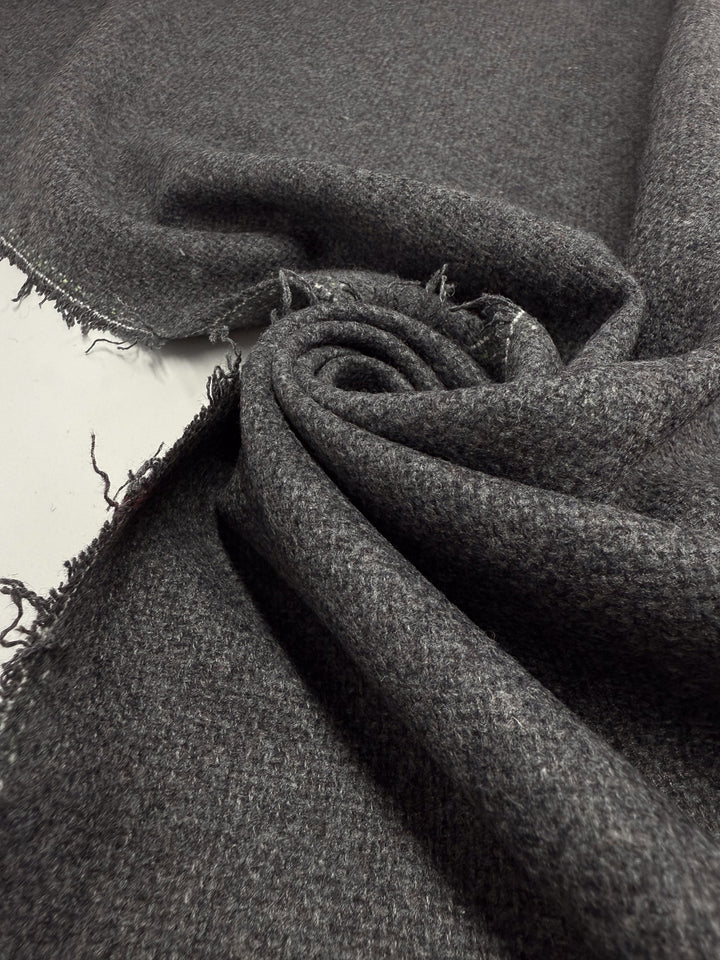 A close-up of Super Cheap Fabrics’ Hopsack Wool - Charcoal (150cm), partially unrolled with textured weave and frayed edges visible on a flat surface.