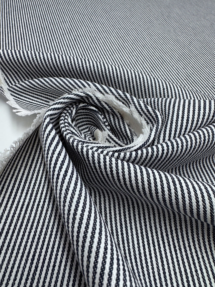 A close-up of Designer Cotton - Pintrack - 150cm by Super Cheap Fabrics, showing its black and white stripes, textured edge, and swirling pattern that highlights the diagonal lines.