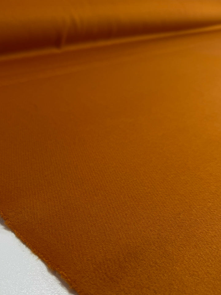 A close-up of Super Cheap Fabrics’ Wool Cashmere - Marmalade - 150cm, unfurled on a flat surface, highlights the luxurious softness, rich texture, and fine weave of this burnt orange fabric.