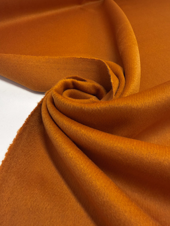 A close-up of Super Cheap Fabrics' Wool Cashmere - Marmalade - 150cm, partially rolled and draped in soft folds, highlights its smooth, slightly fuzzy texture and rich orange hue.