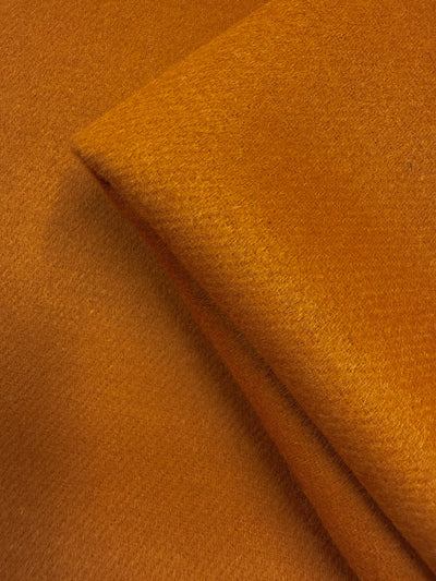 Close-up of Super Cheap Fabrics' Wool Cashmere - Marmalade (150cm), a thick, heavyweight wool fabric in rich orange with a smooth, slightly fuzzy texture and visible fibers for warmth and softness.