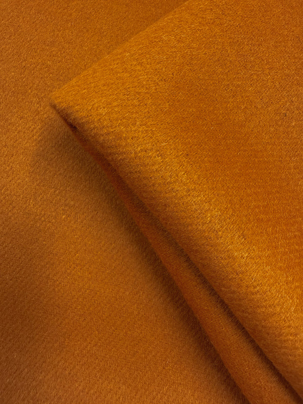 Close-up of Super Cheap Fabrics' Wool Cashmere - Marmalade (150cm), a thick, heavyweight wool fabric in rich orange with a smooth, slightly fuzzy texture and visible fibers for warmth and softness.