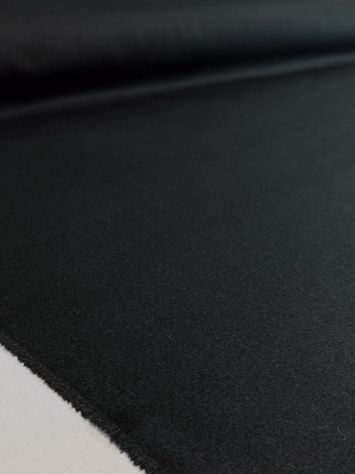 A close-up of Super Cheap Fabrics' Wool Cashmere - Darkest Teal (150cm) shows the smooth, heavy weight fabric spread flat with its edge visible in the foreground.