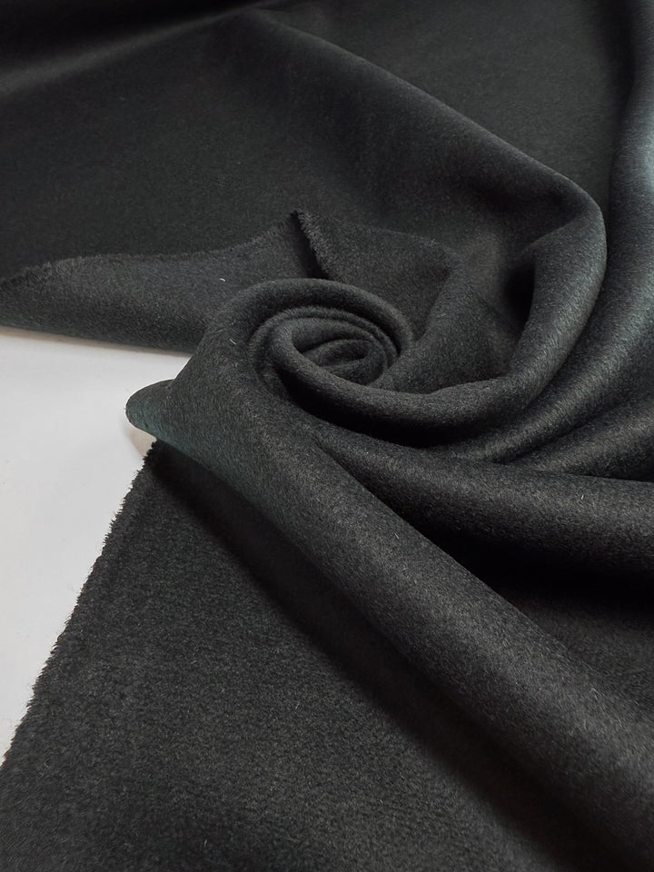 A close-up of Super Cheap Fabrics’ Wool Cashmere in Darkest Teal (150cm), showing its premium, soft texture and unfinished edges, partially rolled into a spiral on a flat surface.