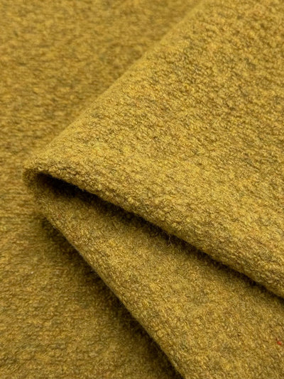 Close-up image of folded mustard Wool Bouclé - Mustard - 135cm by Super Cheap Fabrics, displaying its textured, soft surface. The heavy-weight wool shows fine fibers and subtle variations in shade, highlighting the material's warmth and coziness—perfect for overcoats.