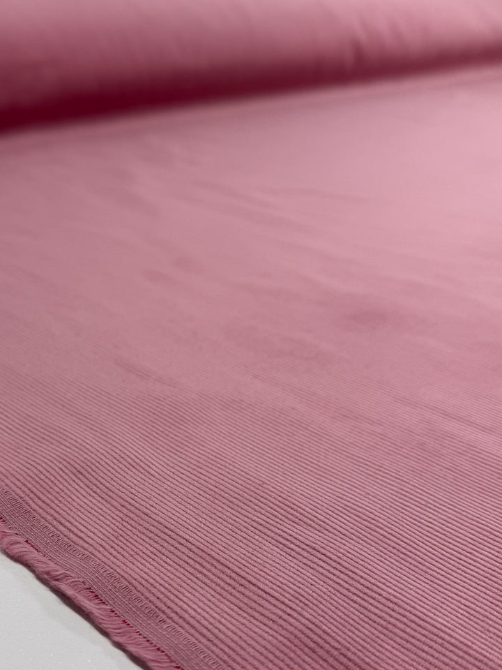 A close-up of Super Cheap Fabrics' Pin Wale Corduroy in Blush (147cm) unrolled on a flat surface, showing its fine ribbed texture—ideal for cozy winter wear.