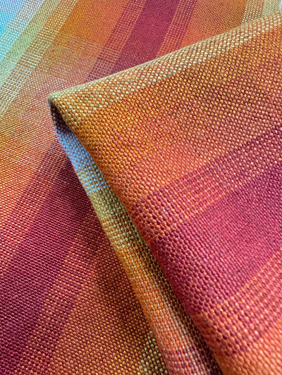 Close-up of "Pure Linen - Morning Sun" by Super Cheap Fabrics, perfect for upholstery. This heavy-weight textile features a warm gradient of orange, red, and yellow tones, folded to showcase its vibrant pattern and texture. Width: 148cm.