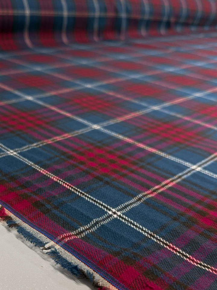 A close-up of Super Cheap Fabrics’ Flannel Tartan - Stirling Rose (145cm), a 100% cotton medium weight plaid flannel in blue, red, and black with white stripes, shown spread out with slightly frayed edges—perfect for shirts.