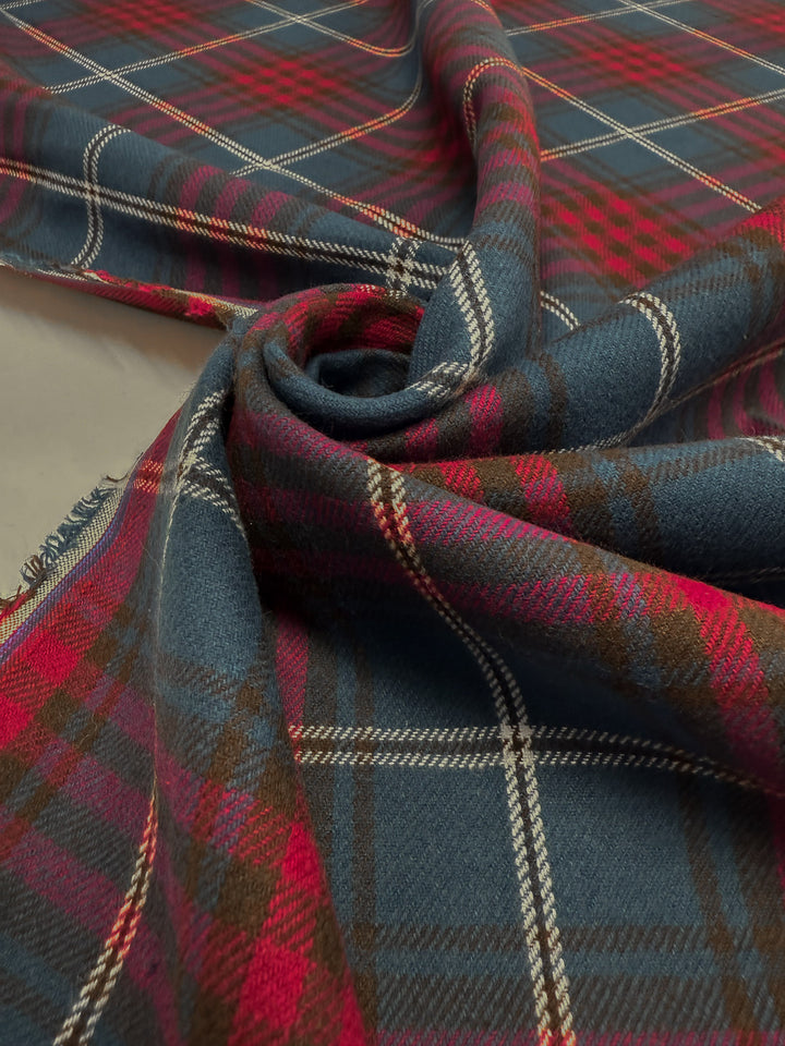A close-up of Super Cheap Fabrics’ Flannel Tartan - Stirling Rose (145cm) shows its blue, red, and brown pattern with white stripes, loosely twisted to highlight the 100% cotton medium-weight texture.
