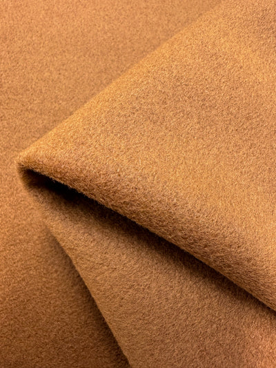 Close-up image of a piece of the Wool Flannel - Honey Ginger by Super Cheap Fabrics folded at an angle, showcasing its soft and fuzzy texture. The fabric's surface appears smooth and evenly colored, emphasizing the material's plush quality, reminiscent of fine textiles from Italy.