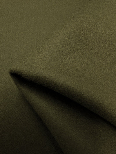 Close-up of Virgin Wool - Dark Dive - 150cm, a piece of olive green, heavy weight fabric with a smooth, soft texture. The fabric is folded over itself, creating gentle, flowing lines and shadowing that accentuates the material's plush and cozy appearance. Crafted by Super Cheap Fabrics in Italy, it exudes quality and elegance.
