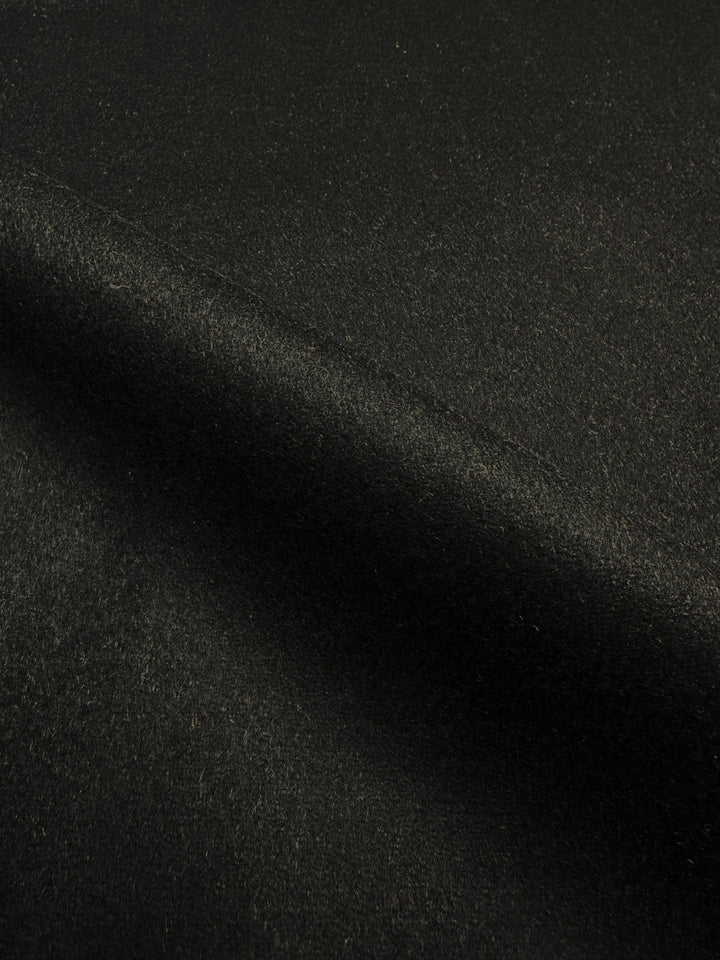 Close-up image of the "Wool Cashmere - New Black - 150cm" fabric by Super Cheap Fabrics. This black heavyweight wool-cashmere blend boasts a soft texture with a slight sheen and features a smooth, even surface. A gentle fold runs diagonally across the image, highlighting the material's thickness and plush quality, making it perfect for crafting outer coats.