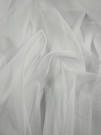 Close-up of crumpled Soft Tulle - White (168cm) by Super Cheap Fabrics, showcasing soft folds and intricate textures. This light and translucent fabric features gentle shadows enhancing its depth.