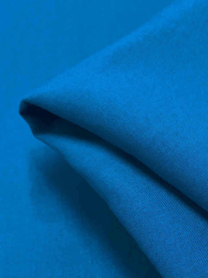 A close-up of the Plain Rayon - Hawaiian by Super Cheap Fabrics showcases a neatly folded corner. Its smooth and slightly soft texture suggests a lightweight material, while the vibrant blue exudes a calming and serene Hawaiian charm.