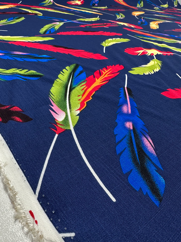 A close-up of Bamboo Rayon - Feather Blue - 150cm by Super Cheap Fabrics shows vibrant green, red, yellow, pink, and blue feather patterns on dark blue fabric—lightweight and perfect for easy sewing projects. Edge visible on the left.