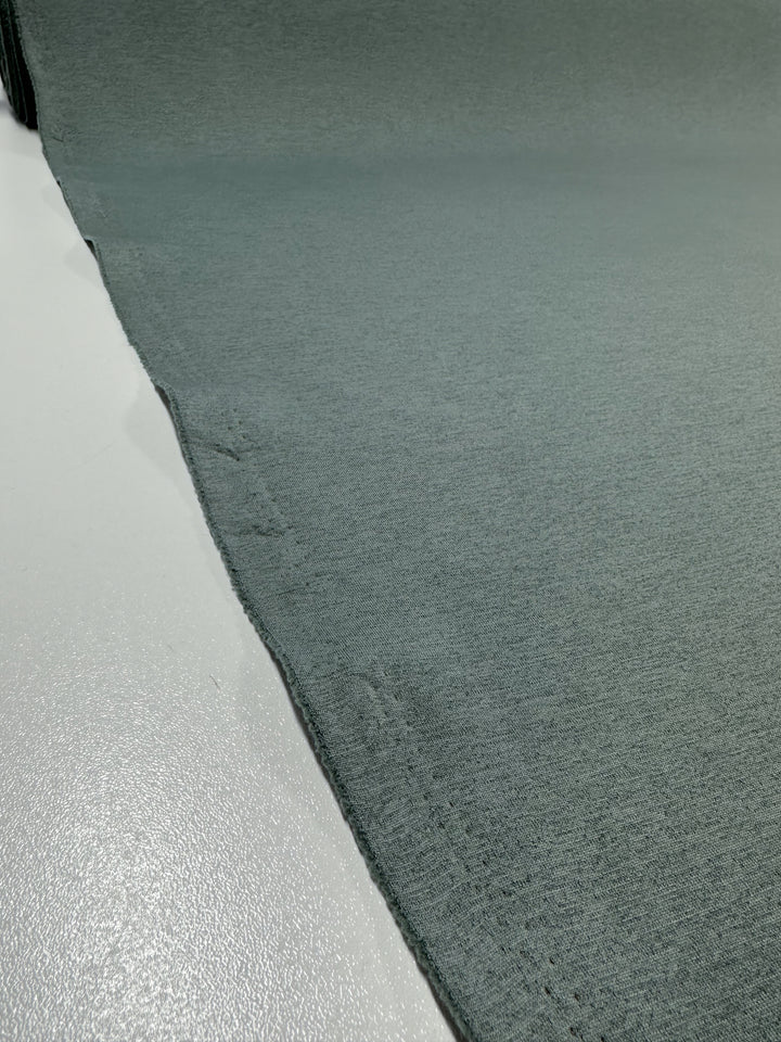 Close-up of a matte, gray Scuba Knit from Super Cheap Fabrics, laid out on a flat surface. The Scuba Knit - Mermaid - 165cm extends diagonally from the bottom left corner to the top right, with the edge slightly frayed and uneven. The texture of this stretchy textile is smooth with subtle weave patterns visible.