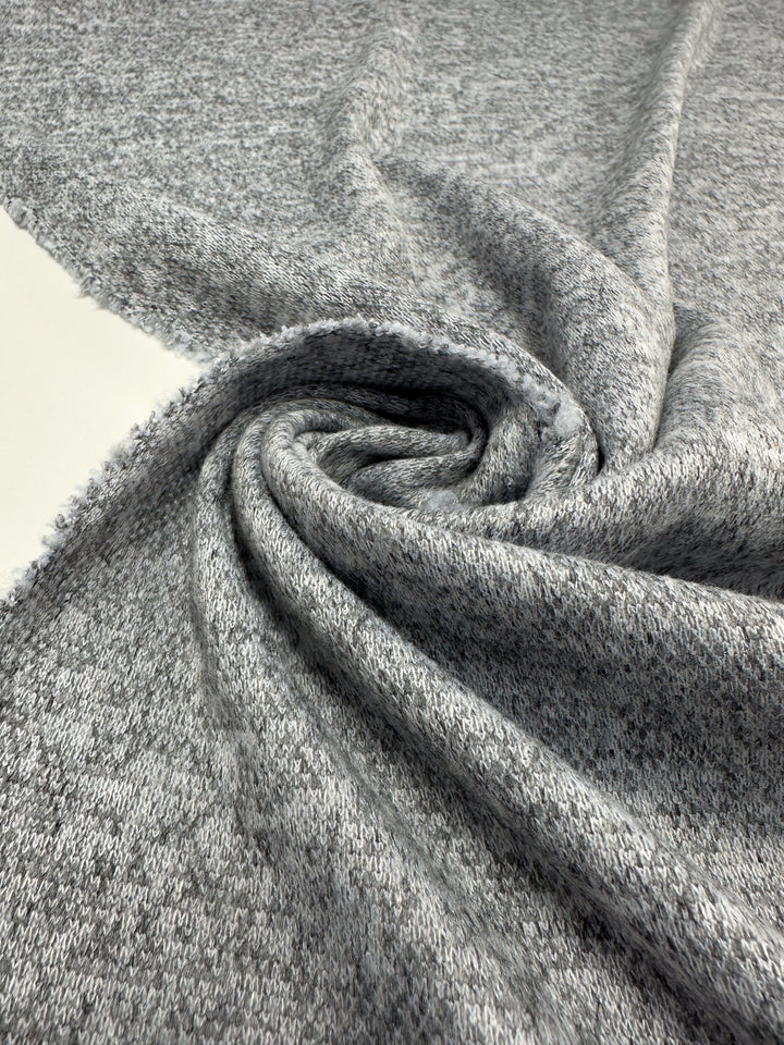 A close-up of Super Cheap Fabrics’ Textured Knit - Grey Marle - 155cm shows its soft, medium-weight fabric with a subtle pattern, gathered and twisted for maximum comfort.