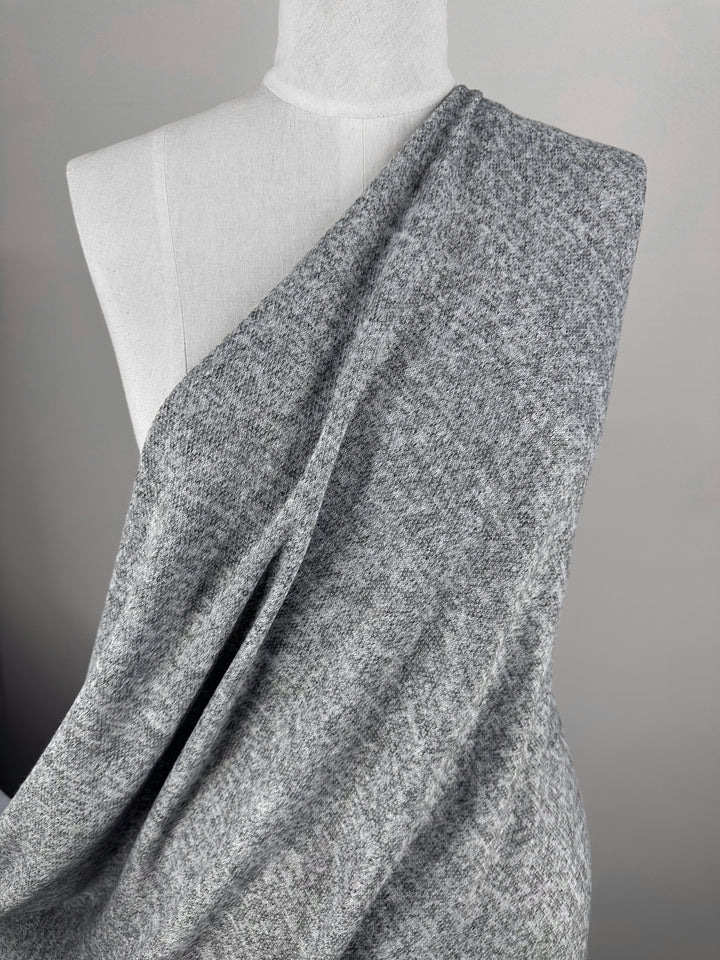 A close-up of Super Cheap Fabrics' Textured Knit - Grey Marle (155cm) draped diagonally over a dress form shoulder, showcasing its soft, heather gray texture against a neutral background.