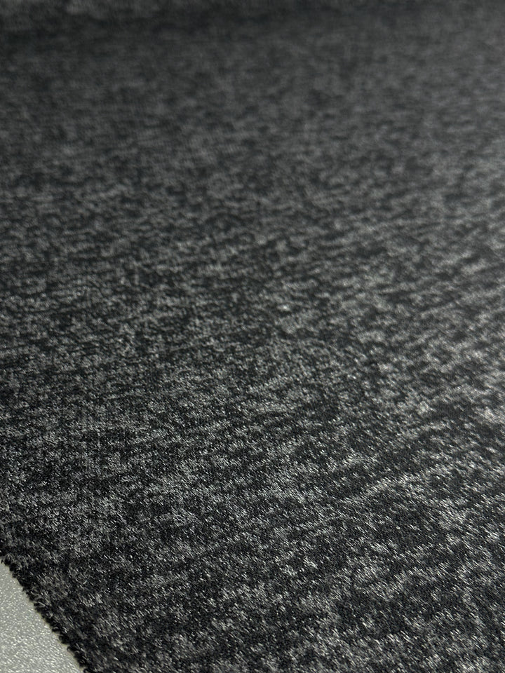 A close-up of Super Cheap Fabrics' Textured Knit - Black Marle (150cm) shows the soft, stretchy polyester fabric with a marled pattern, highlighting its cozy texture and stylish dark gray finish.