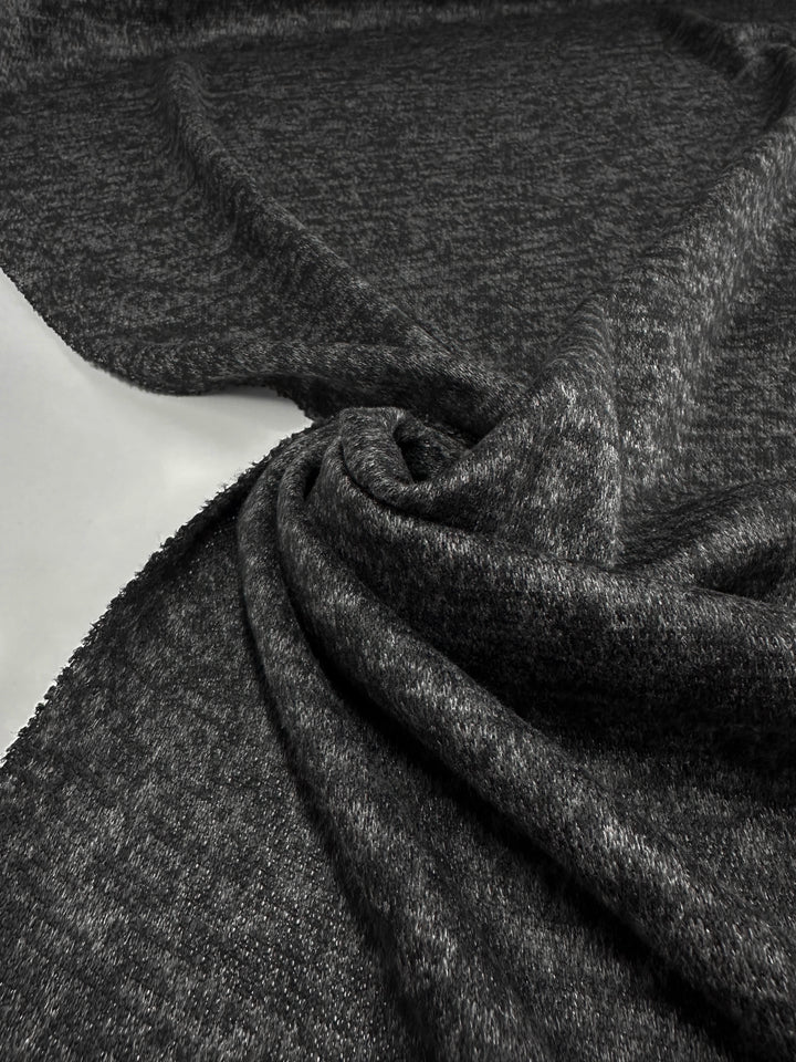 A close-up of Super Cheap Fabrics’ Textured Knit - Black Marle - 150cm, spread out and gently twisted to show its soft texture and slight stretch—an elegant example of versatile knit fabric.