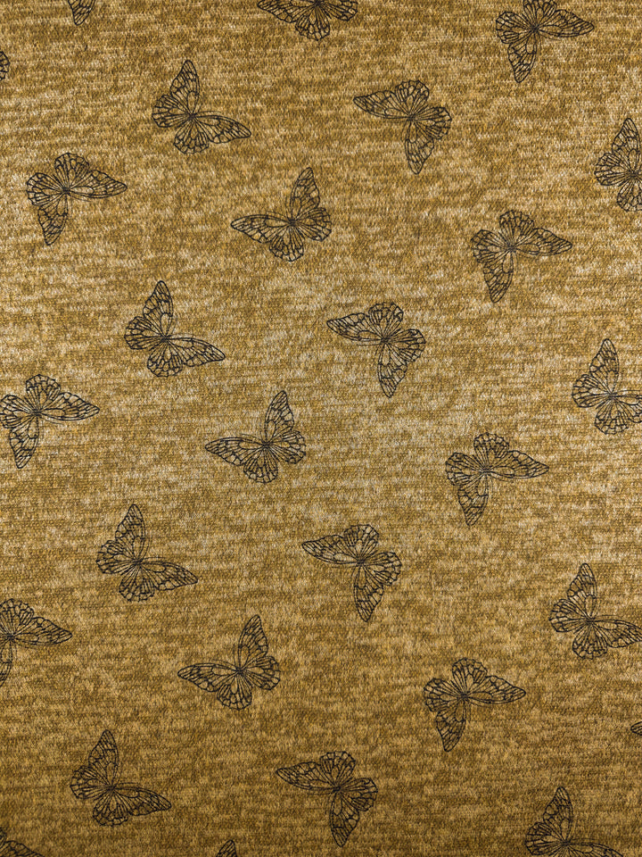 Super Cheap Fabrics' Textured Knit - Amber Gold Butterfly - 150cm features a brown knit with black outlined butterflies in a repeating pattern, accented by hints of amber gold for a charming, medium weight fabric.