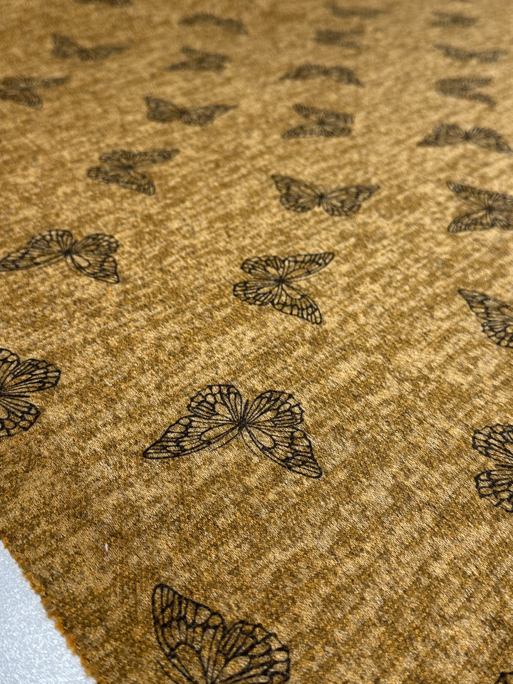 Super Cheap Fabrics' Textured Knit - Amber Gold Butterfly (150cm) features a medium-weight brown knit with a repeating black butterfly pattern, evenly spaced across an amber gold surface, highlighting its textured design.
