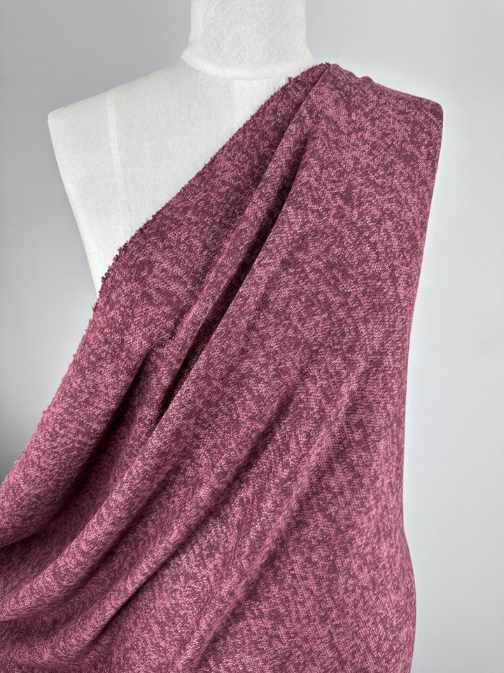 A white mannequin displays Super Cheap Fabrics’ Textured Knit - Tulipwood, a soft, medium-weight maroon heather fabric draped over one shoulder, set against a plain light gray background.