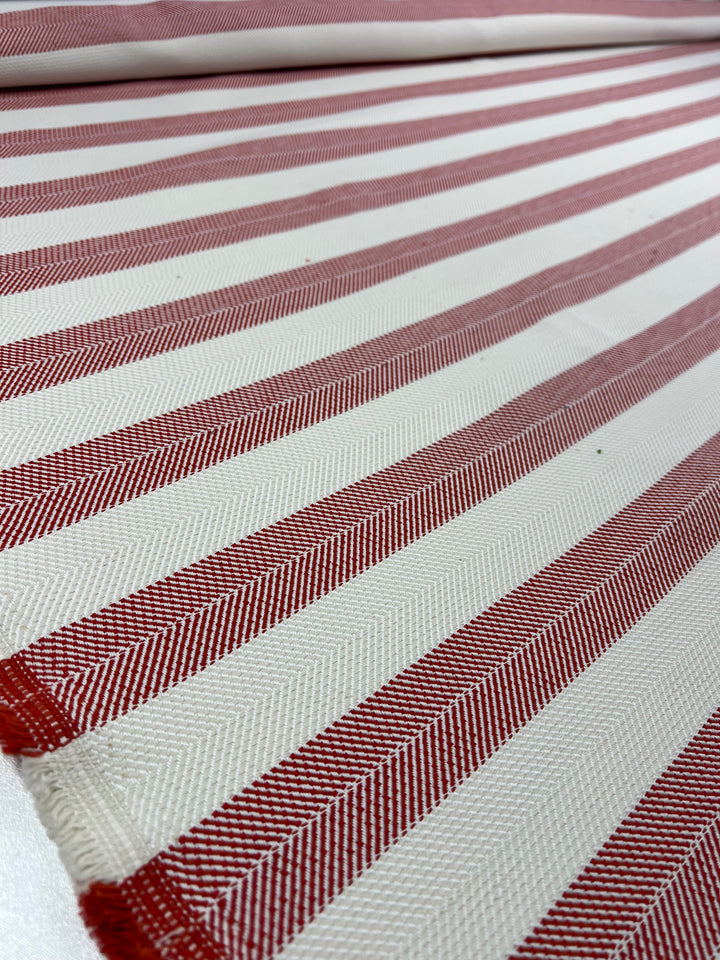 A close-up of Super Cheap Fabrics' Upholstery Herringbone - Terracotta - 140cm with a pattern of red and white stripes. The stripes alternate in color, creating a pleasing, linear design. The texture appears to be woven, with a diagonal herringbone pattern visible within the durable, stylish fabric.